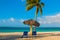 Playa Esmeralda, Holguin, Cuba. Caribbean sea: two sun loungers, umbrella, palm tree on the beach, on the background of the turquo