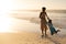 Playful african american young woman holding son\\\'s hands and spinning him at beach against sky