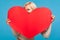 Playful blond girl peeping from big paper red heart in her hands, saint valentines day celebration, love and fondness