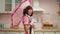 Playful charming Asian female in maid cosplay costume posing with pink umbrella