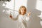 Playful cheerful little beautiful girl with blonde curly hair plays with toy deer, dressed in festive white dress, ready