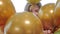 Playful cheerful young girl looks out from a bunch of balloons and smiling