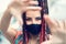 Playful cool rebel funky hipster young girl with face mask and crazy hair taking selfie on street