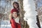 Playful couple in the snow hiding behind a tree trunk