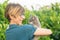 Playful domestic cat held and cuddled by smiling woman with eyeglasses. Outdoor setting in green home garden. Shallow depth of fie