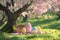 A playful Easter card concept with a group of colorful, cartoon-style Easter eggs having a picnic under a cherry blossom tree,