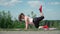 Playful Fat Man with Long Hair Does Gymnastics for Weight Loss Outdoors. Funny Overweight Guy Depicting a Girl Engaged In Fitness