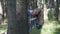 Playful funny smiling teenage woman having fun in the forest fooling around and hiding beyond tree -