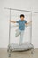 Playful indian boy standing on a garment rack with metal frame and wheels.