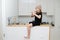 Playful little girl in a beige hat playing with a flute, sitting on a high table