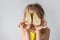 Playful little girl in sunny yellow dress hiding her eyes jokingly behing the halves of cutted pear. Close up studio