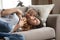 Playful little preschool daughter lying on sofa with smiling mother.