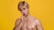 Playful shirtless blonde guy shooting to camera with hand and smiling, winking to camera, orange studio background