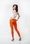 Playful smiling young woman in orange pants posing on neutral ba