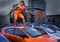 Playful stylish girl in orange overalls standing on car roof in the parking lot