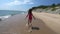 Playful young girl, kid running barefoot in pink swimwear on sandy beach in summer vacation, sea waves approaching the shore