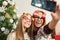 Playful young woman and teenage daughter posing and taking a selfie in front of a Christmas tree