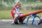 Playground conflicts. Small cute young blond child girl sits moody, angry and offended on see- saw swing on bright green blurred b