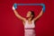 Pleasant active woman doing bodyweight training with resistance rubber band on red background with copy space for ads