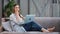 Pleasant casual barefoot girl sitting on couch with laptop enjoying break. Wide shot on RED camera