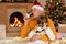 Pleasant little girl drinking tea with her caring grandfather while sitting on floor in festive living room near fir tree and