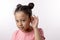 Pleasant little girl wearing stylish pink dress is touching her ears