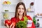 Pleasant looking female model with cheerful expression holds fresh vegetables which she bought in grocer`s shop, stands near opene