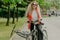 Pleasant looking young woman in sunglasses, rides sport bicycle, stops for break, enjoys beauty of nature, calm atmosphere, laughs