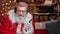 Pleasant male Santa Claus listening music in headphones use smartphone. Medium shot on RED camera