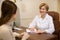 Pleasant mature smiling female doctor sitting in front of laptop and meeting with her patient