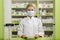 Pleasant professional young female pharmacist with surgical mask smiling