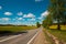 Pleasant sunny summer landscape: old blue sky and clouds, green grass, yellow dandelion rapeseed flowers on a meadow and a highway