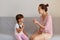 Pleasant young adult speech therapist teaching little female kid right sounds pronunciation, professional physiotherapist working