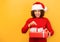 Pleasantly excited happy woman holds in hands christmas gift. woman in santa claus hat on orange background, smiling