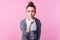 Please be silent. Portrait of brunette teen girl showing hush be quiet gesture with finger on lips. isolated on pink background