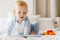 Pleased blonde baby boy looking at tablet computer while playing on bed