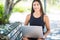 Pleased brunette latin woman isitting on bench in park and using laptop computer