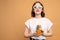 Pleased european girl in white sunglasses holds pineapple in her hands and looking at the camera, orange wall on the