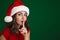 Pleased girl in Santa Claus hat showing silence gesture on camera