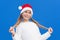 Pleased girl in white sweater and Santa hat holding pigtails smiling away isolated on blue background