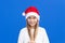 Pleased girl in white sweater and Santa hat holding pigtails smiling away isolated on blue background