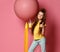 Pleased and happy young lady, teen girl in jeans and yellow t-shirt with glass of yellow juice stands at big pink balloon