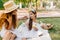 Pleased lady in hat and golden ring telling something to daughter which holding green apple. Outdoor portrait of smiling