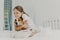 Pleased little girl plays with pet, embraces dog and keeps eyes closed from pleasure, dressed in nightclothes, poses on bed after