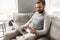 Pleased modern man 30s in casual wear sitting on sofa in living