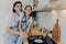 Pleased mother with little helping daughter near cooker, prepare breakfast for whole family, fry eggs on pan, pose in modern