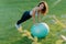 Pleased slim woman leans at fit ball, dressed in active wear, has gymnastic exercises on green lawn, enjoys sport and favorite