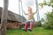 Pleased toddler girl wearing red kids gumboots riding on handmade rustic swing