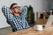 Pleased unshaven man in eyeglasses resting while working with laptop