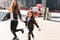 Pleased woman in black pants and sneakers spending time with daughter running across the town with red bus on background